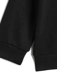 Tessuto di felpa nero a coste con una finitura testurizzata. I polsini e l'orlo sono anch'essi a coste, offrendo una vestibilità aderente.