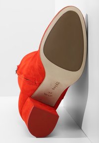 Bottine en daim rouge avec talon bloc, semelle beige, taille 37, vue inclinée de la semelle sur fond blanc.