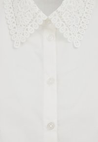 Biała bluzka z ozdobnym koronkowym kołnierzem, zapięciem na guziki i gładką fakturą materiału; koronka ma misterny kwiatowy wzór.