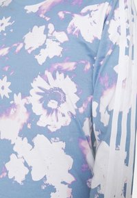 Blå sweatshirt med blommönster i rosa och vita färger, prydd med en vit Adidas-logotyp och tre vita vertikala ränder på ärmarna.