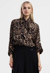 Blusa in stampa leopardata marrone e nera, con scollo annodato e maniche ampie, abbinata a una gonna nera. Tessuto morbido e fluido.