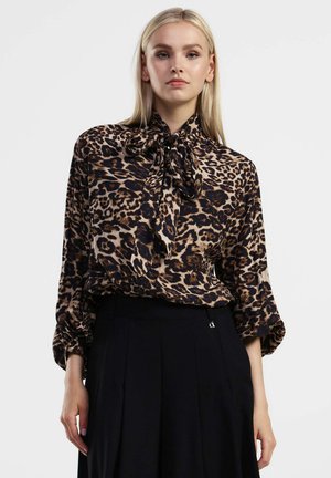 Blusa in stampa leopardata marrone e nera, con scollo annodato e maniche ampie, abbinata a una gonna nera. Tessuto morbido e fluido.