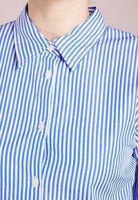 Blå och vit randig skjorta med klassisk krage, med vertikala ränder, knäppning och slät tygtextur.