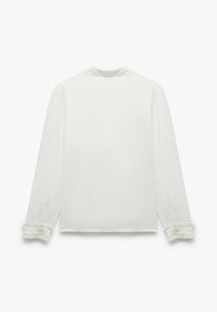 Vit långärmad blus med en mjuk textur, klassisk krage och volangdetaljer vid de knappade manschetterna. Enkel och elegant design.
