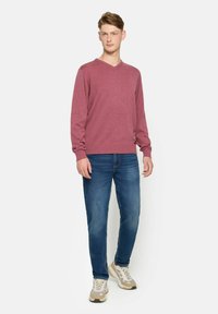 Pulover V cu gât, de culoare bordo, realizat dintr-un material moale, asortat cu blugi blue și adidași în culori neutre. Croială simplă cu detalii cu manșete ribbate.