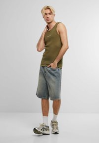 Top estivo in maglia verde oliva con un motivo testurizzato, abbinato a pantaloni shorts in denim azzurro chiaro. Indossato con calze bianche e scarpe da ginnastica in tono argento.