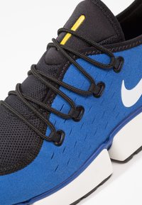 Modré nubukové a černé síťované tenisky s šněrováním, s žlutým akcentem, bílým logem, texturovaným povrchem a bílou mezipodešví.