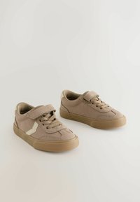 Beige ruskindsko med en tan gummisål. Har både snørebånd og en velcro-rem. Sideaccent i en lysere tone.