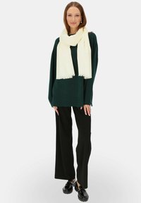 Zielony oversize'owy sweter, kremowy szalik, czarne szerokie spodnie i błyszczące czarne buty. Miękka tekstura, casualowy design, gładki, bez wzorów.