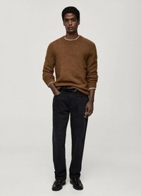 Brauner Strickpullover mit weißem Besatz, kombiniert mit dunkelblauen, geraden Hosen und schwarzen Slippern. Das Outfit besteht aus einem strukturierten Stoff.