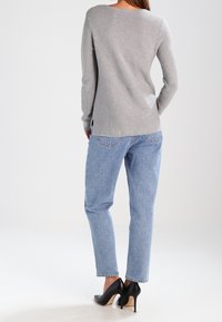 Hellgrauer Langarmoberteil mit rundem Ausschnitt, kombiniert mit hellblauen Straight-Leg-Jeans und schwarzen High Heels.