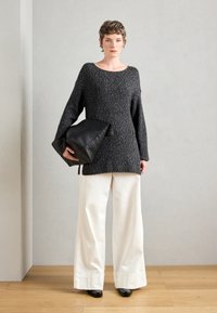Prevelik temno sivi pleten sweater z širokimi rokavi, v kombinaciji z off-white širokimi hlačami in črno usnjeno torbico. Gladke teksture.