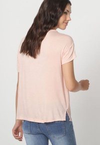 Camiseta de manga corta rosa claro con un ajuste holgado, textura suave, aberturas laterales y dobladillo redondeado, combinada con unos vaqueros de mezclilla.