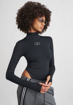 Juodas ilgų rankovių bodysuit'as su uždarais kaklu ir šoninėmis išpjovomis, pasižymintis paprastu baltu logotipu ant krūtinės. Lygi, elastinga medžiaga.