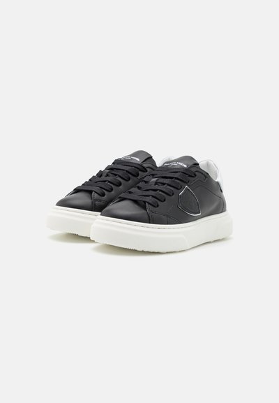Baskets en cuir noir avec semelle en caoutchouc blanche, dotées d'un bout rond, d'un laçage et d'un accent logo argenté sur le côté.