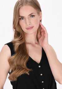 Top senza maniche nero con scollo a V e dettagli di bottoni dorati, indossato da una modella con capelli castano chiaro mossi, di lunghezza fino alle spalle.