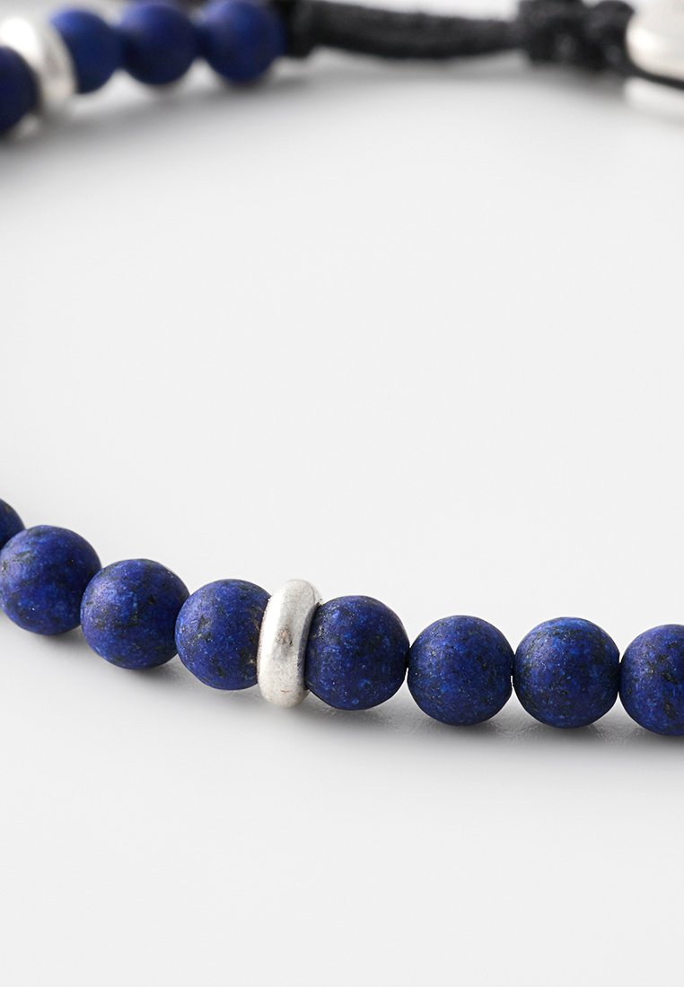 Niebieskie koraliki lapis lazuli oraz jedna metaliczna srebrna przekładka na czarnym sznurku, o gładkiej teksturze i okrągłym kształcie.