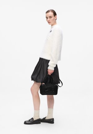 Fluffy white sweater, black pleated skirt, black handbag with raised lettering, and black loafers worn with cream socks.