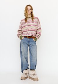 Pletený svetr s růžovo-fialovým vzorem, zelené manžety; světle modré džíny volnějšího střihu; béžové boty s kožíškem a šňůrkami.