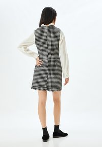 Sorte og hvide houndstooth-kjole med frynset kant, tætsiddende liv og høj hals. Båret over en cremet langærmet top og parret med sorte sko.