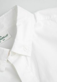 Biała bawełniana koszula z klasycznym kołnierzem, wyposażona w metkę i dwa guziki przy szyi, gładka faktura oraz zakładka przy kołnierzu.