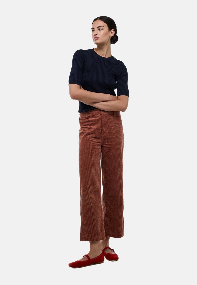 Haut court à rayures côtelées bleu marine, pantalon large en velours côtelé couleur rouille et ballerines rouges. Texture remarquable et coupe ajustée du haut.