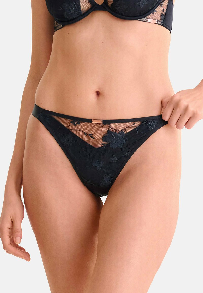 String noir en dentelle florale, avec une texture semi-transparente et une taille lisse ornée d'un petit accent métallique.