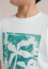 T-shirt di cotone azzurro chiaro con una grafica di palma verde e il testo "SUNSHINE STATE OF MINE." Morbido al tatto, design a collo rotondo.