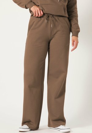 Braune Sweatpants mit lockerer Passform, Kordelzugbund und seitlichen Taschen. Kombiniert mit weißen Turnschuhen für einen Kontrast. Weicher, strukturierter Stoff.