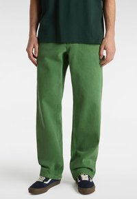 Green denim pants with a relaxed fit, featuring side pockets and subtle stitching details, paired with blue sneakers and a dark shirt.