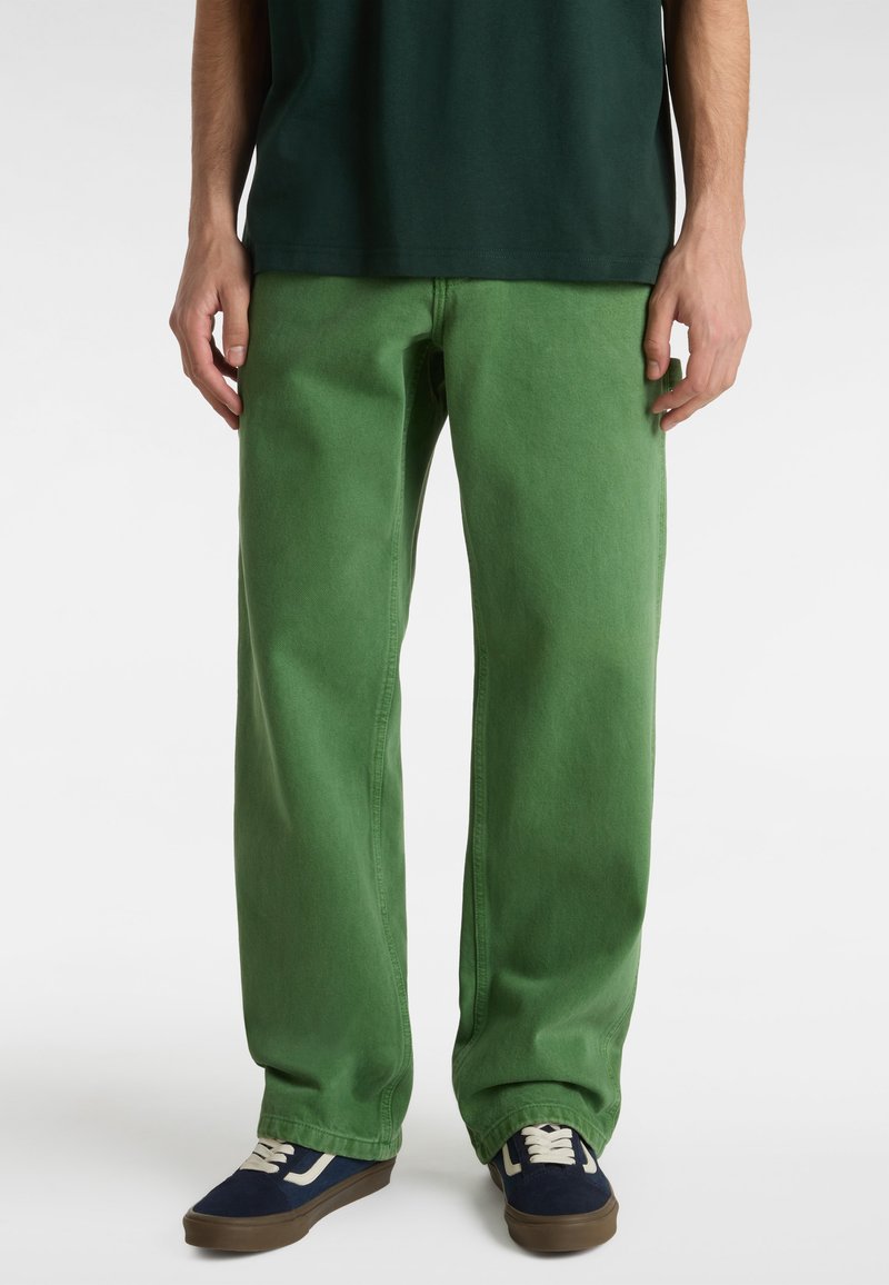 Green denim pants with a relaxed fit, featuring side pockets and subtle stitching details, paired with blue sneakers and a dark shirt.