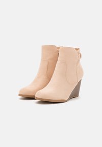Bottines beiges en daim avec un talon compensé, dotées d'une texture lisse, de coutures minimales, d'un bout arrondi et d'une fermeture éclair.