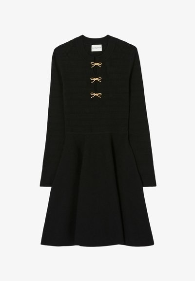 Robe tricot noir à manches longues avec jupe évasée et trois petits boutons en forme de nœud en or le long de l'encolure.