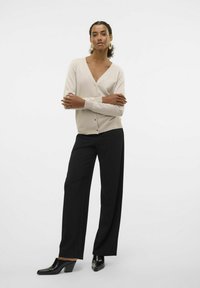 Cardigan beige clair avec un col en V et des boutons, associé à un pantalon noir taille haute et des chaussures à talons blocs noires brillantes.