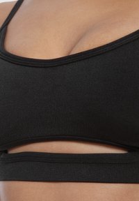 Zwarte sport-bh met ribbelstructuur, V-hals ontwerp en uitsnijding aan de onderkant. Zachte stof met elastische ondersteuning.