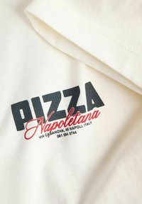 Λευκό βαμβακερό T-shirt με μεταξοτυπία λογότυπου που αναγράφει "PIZZA Napoletana" με έντονα μαύρα και κόκκινα γράμματα και τη διεύθυνση ενός εστιατορίου από κάτω.