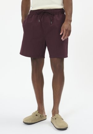 Pantaloni elasticizzati bordeaux con un motivo testurizzato, vita regolabile con coulisse, tasche laterali e vestibilità rilassata. Calzature: mocassini in suede color tan.
