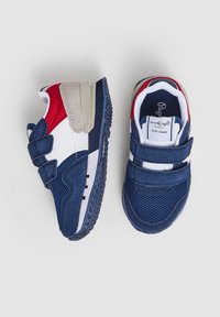 Tossut tummansinisiä punaisilla, valkoisilla ja beigeillä yksityiskohdilla, joissa on tarrakiinnitys, verkkomaiset paneelit ja teksturoitu kumipohja.