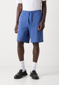 Shorts din bumbac bleu cu talie elastică și cordon ajustabil. Prezintă buzunare laterale și un croi lejer. Asortați cu șosete albe și pantofi negri.