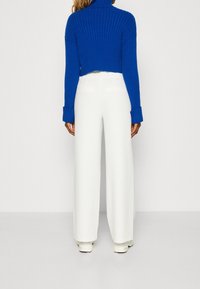 Blauwe geribbelde coltrui, cropped ontwerp, gecombineerd met witte wijde broekspijpen. De outfit heeft lange mouwen en opgevouwen manchetten.