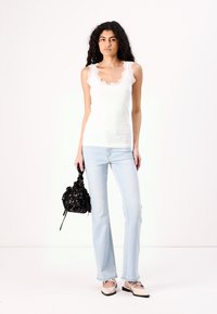 White ribbed tank top with lace trim, light blue flared jeans, and black bag with floral design. Footwear features a two-tone pattern.