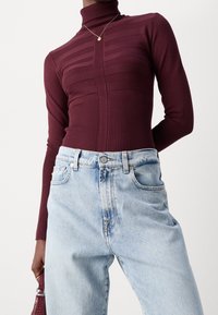 Haut col roulé bordeaux avec texture côtelée et rayures verticales, associé à un jean en denim bleu clair taille haute et un petit sac à main.