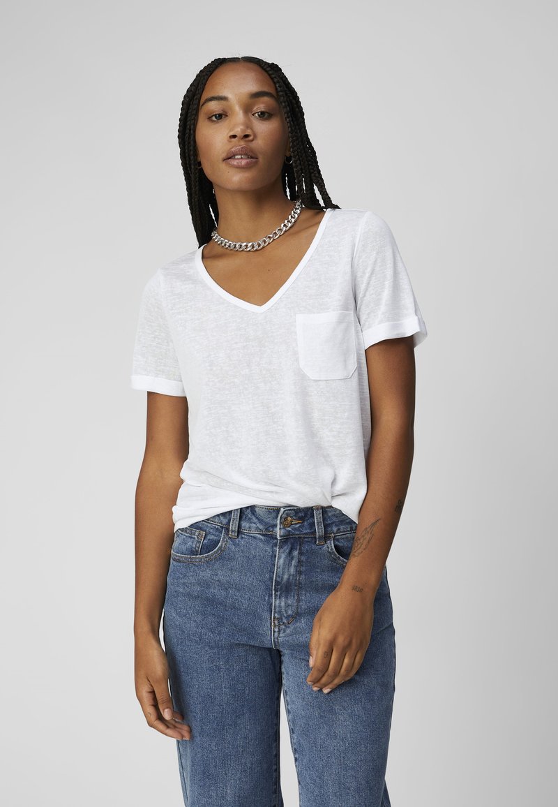 White short-sleeve V-neck t-shirt with a left chest pocket, paired with blue high-waisted jeans. Soft texture, relaxed fit.