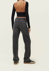 Top corto negro de manga larga con la espalda descubierta, combinado con jeans grises de tiro alto y corte relajado, con bolsillos traseros. Zapatillas negras y grises.