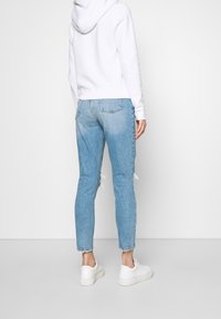 Sudadera blanca con capucha combinada con jeans skinny desgastados de color azul claro, con dobladillos deshilachados y un lavado mínimo. Zapatillas blancas.