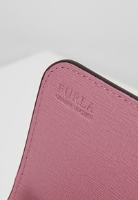 Gros plan sur un coin en cuir véritable rose texturé avec des bords cousus et le nom de la marque Furla embossé.