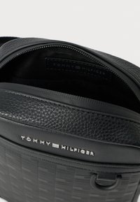 Zaino in pelle nera con superficie testurizzata, chiusura con zip e logo Tommy Hilfiger. L'interno presenta un compartimento foderato e un'etichetta con il marchio.