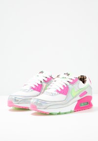 Bílé tenisky se stříbrnými akcenty, růžovými a zelenými detaily a podšívkou s leopardím vzorem. Obsahují průhlednou podrážku a klasický design na šněrování.