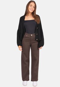 Cardigan noir en maille avec manches longues, orné de gros boutons dorés. Associé à un pantalon marron taille haute et des baskets blanches.