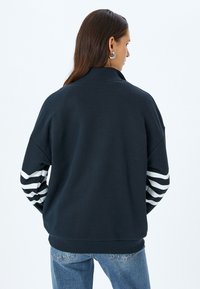 Felpa blu navy con colletto alto, vestibilità ampia e maniche a righe bianche. Realizzata in cotone con una texture morbida.